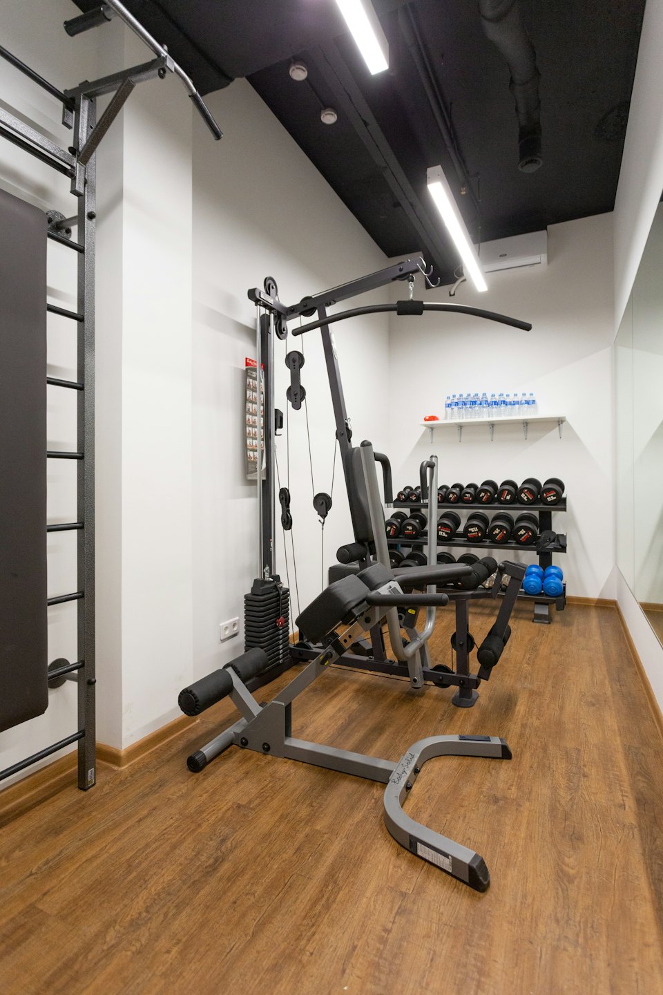Leerer privater Fitnessraum mit Multifunktionsturm, Hanteln und Kettlebells.