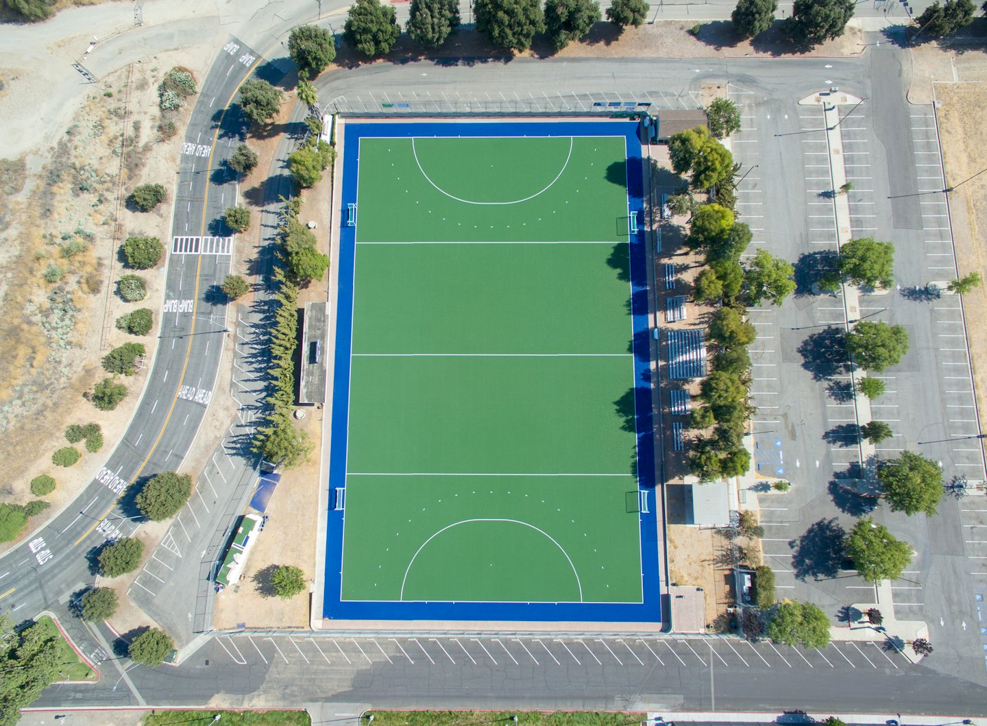Grünes Hockeyfeld, umgeben von Parkplätzen.