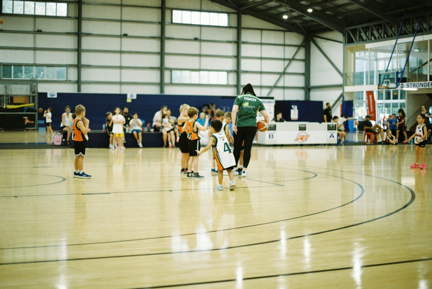 Ein Basketballtrainer spricht mit Kindern auf einem Hallenplatz.